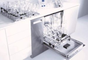 Sleek and modern laboratory glassware washer, Miele PG 8583 CD, with its door open, displaying a loaded rack full of sparkling clean laboratory glassware. The washer is set against a minimalistic white lab counter, enhancing the clean, efficient design ideal for high-purity applications. This image showcases the equipment's capability to handle delicate and critical cleaning processes in scientific research environments.