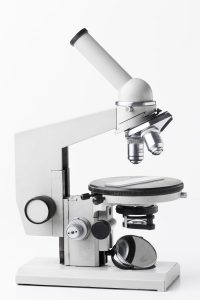 A close-up photo of a modern laboratory microscope on a white background. The microscope is equipped with multiple lenses, fine adjustment knobs, and a stage for placing specimens, highlighting its functionality for detailed scientific research and examination.